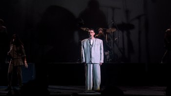 Movie still from “Stop Making Sense” (1984), directed by Jonathan Demme – A man standing on a stage holding a microphone; Wide shot, Low angle