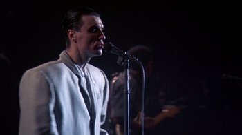 Movie still from “Stop Making Sense” (1984), directed by Jonathan Demme – A man in a white jacket singing into a microphone; Close Up shot, Low angle
