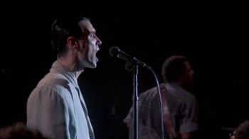 Movie still from “Stop Making Sense” (1984), directed by Jonathan Demme – A man is singing into a microphone on a stage; Close Up shot, Low angle