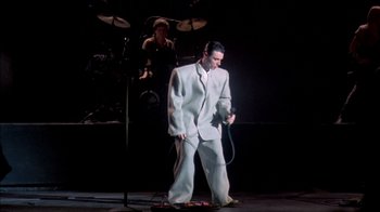 Movie still from “Stop Making Sense” (1984), directed by Jonathan Demme – A man in a white suit standing on a stage; Wide shot, Low angle