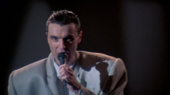 Movie still from “Stop Making Sense” (1984), directed by Jonathan Demme – A man in a white suit is holding a microphone; Close Up shot, Low angle