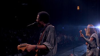 Movie still from “Stop Making Sense” (1984), directed by Jonathan Demme – A man with a microphone and a guitar in front of an audience; Medium shot, Low angle