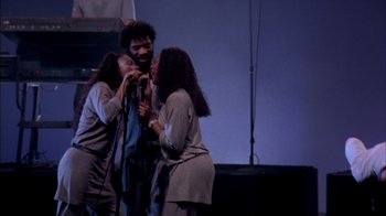 Movie still from “Stop Making Sense” (1984), directed by Jonathan Demme – A man and two women singing on a stage; Medium shot, High angle