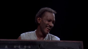 Movie still from “Stop Making Sense” (1984), directed by Jonathan Demme – A person sitting at a keyboard; Close Up shot, High angle
