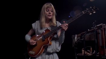 Movie still from “Stop Making Sense” (1984), directed by Jonathan Demme – A woman holding a guitar in front of a microphone; Medium shot, Low angle