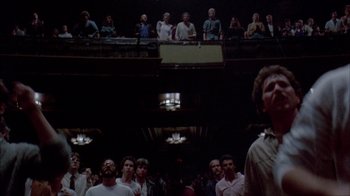 Movie still from “Stop Making Sense” (1984), directed by Jonathan Demme – A group of people standing in a room with lights on; Wide shot, Low angle