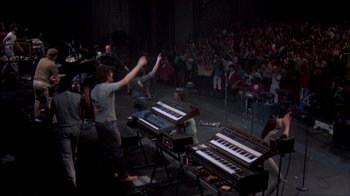 Movie still from “Stop Making Sense” (1984), directed by Jonathan Demme – A group of young people standing in front of keyboards; Wide shot, High angle