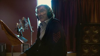 Movie still from “Stories We Tell” (2012), directed by Sarah Polley – An older man wearing headphones in front of a microphone; Medium shot, Low angle