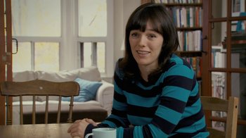 Movie still from “Stories We Tell” (2012), directed by Sarah Polley – A woman sitting at a table with a coffee mug; Medium shot, Over the shoulder angle