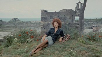 Movie still from “Stories We Tell” (2012), directed by Sarah Polley – A woman sitting on the ground in front of an abandoned building; Wide shot, High angle