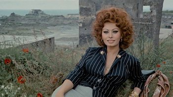 Movie still from “Stories We Tell” (2012), directed by Sarah Polley – A woman sitting on the ground in front of a field; Medium shot, High angle