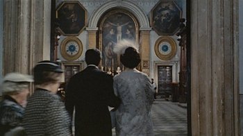 Movie still from “Stories We Tell” (2012), directed by Sarah Polley – A man and a woman holding hands in front of a painting; Wide shot, Low angle