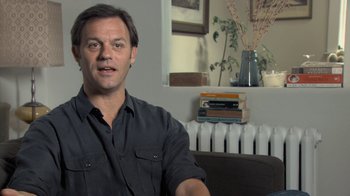 Movie still from “Stories We Tell” (2012), directed by Sarah Polley – A man sitting in front of a window in a living room; Medium shot, Low angle