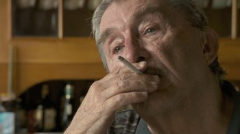 Movie still from “Stories We Tell” (2012), directed by Sarah Polley – An older man smoking a cigarette while looking at the camera; Close Up shot, Over the shoulder angle