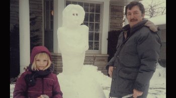 Movie still from “Stories We Tell” (2012), directed by Sarah Polley – A man and a little girl standing next to a snowman; Medium shot, High angle