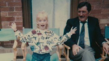 Movie still from “Stories We Tell” (2012), directed by Sarah Polley – A little girl is smiling for a picture with her father; Medium shot, High angle