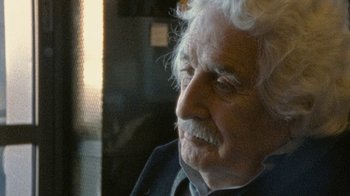 Movie still from “Stories We Tell” (2012), directed by Sarah Polley – An older man with white curly hair looking out a window; Close Up shot, Over the shoulder angle