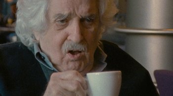 Movie still from “Stories We Tell” (2012), directed by Sarah Polley – An older man holding a coffee cup in his hands; Close Up shot, Over the shoulder angle