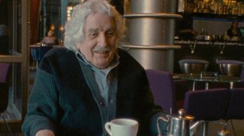 Movie still from “Stories We Tell” (2012), directed by Sarah Polley – An older man sitting at a table with a cup of coffee; Close Up shot, High angle