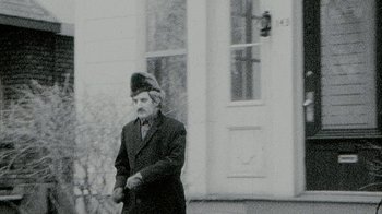 Movie still from “Stories We Tell” (2012), directed by Sarah Polley – An older man wearing a fur hat standing in front of a building; Medium shot, Low angle
