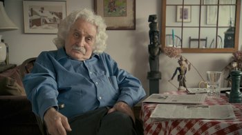 Movie still from “Stories We Tell” (2012), directed by Sarah Polley – An older man sitting in a chair in front of a table; Close Up shot, Over the shoulder angle