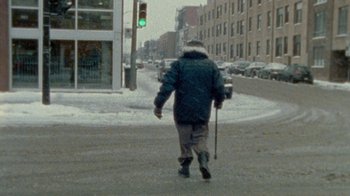 Movie still from “Stories We Tell” (2012), directed by Sarah Polley – A man walking down a street with a cane; Wide shot, High angle
