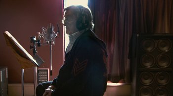 Movie still from “Stories We Tell” (2012), directed by Sarah Polley – An older man sitting in front of a microphone in a room; Medium shot, Low angle