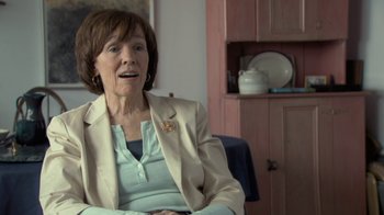 Movie still from “Stories We Tell” (2012), directed by Sarah Polley – An older woman sitting in a chair in a room; Close Up shot, Over the shoulder angle