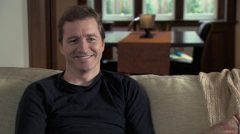 Movie still from “Stories We Tell” (2012), directed by Sarah Polley – A man sitting on top of a couch in a living room; Close Up shot, High angle