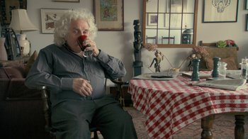 Movie still from “Stories We Tell” (2012), directed by Sarah Polley – An older man sitting at a table drinking a cup of coffee; Medium shot, Over the shoulder angle