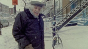 Movie still from “Stories We Tell” (2012), directed by Sarah Polley – An older man in a winter coat and hat; Medium shot, High angle