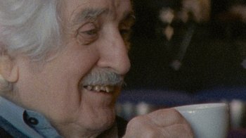 Movie still from “Stories We Tell” (2012), directed by Sarah Polley – An old man with a mustache is holding a cup; Close Up shot, Over the shoulder angle