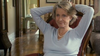 Movie still from “Stories We Tell” (2012), directed by Sarah Polley – An older woman sitting in a chair with her hands behind her head; Close Up shot, Over the shoulder angle