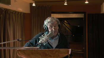 Movie still from “Stories We Tell” (2012), directed by Sarah Polley – An older man wearing headphones and a microphone in a room; Medium shot, Low angle
