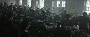 Movie still from “All Quiet on the Western Front” (2022), directed by Edward Berger – A group of people sitting around sewing machines in a room; Wide shot, High angle
