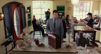 Movie still from “Stranger Than Fiction” (2006), directed by Marc Forster – A man holding a briefcase standing in front of a counter; Medium shot, Over the shoulder angle