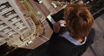Movie still from “Stranger Than Fiction” (2006), directed by Marc Forster – A man on a cell phone looking down at a busy street; Wide shot, Overhead angle