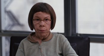 Movie still from “Stranger Than Fiction” (2006), directed by Marc Forster – An older woman wearing glasses sitting in front of a window; Close Up shot, Over the shoulder angle