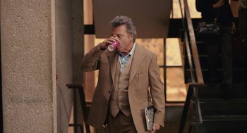 Movie still from “Stranger Than Fiction” (2006), directed by Marc Forster – A man in a brown suit drinking from a pink cup; Medium shot, Over the shoulder angle
