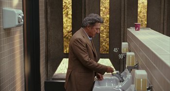 Movie still from “Stranger Than Fiction” (2006), directed by Marc Forster – A man in a brown suit is washing his hands; Medium shot, Over the shoulder angle
