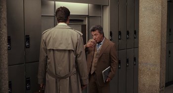 Movie still from “Stranger Than Fiction” (2006), directed by Marc Forster – A man in a brown suit is standing next to another man in a brown suit; Medium shot, Over the shoulder angle