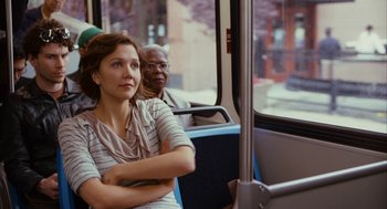 Movie still from “Stranger Than Fiction” (2006), directed by Marc Forster – A woman sitting on a public transit bus with her arms crossed; Medium shot, Over the shoulder angle