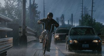 Movie still from “Stranger Than Fiction” (2006), directed by Marc Forster – A man riding a bike down a street in the rain; Wide shot, Low angle