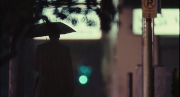 Movie still from “Stranger Than Fiction” (2006), directed by Marc Forster – A person holding an umbrella while standing in the rain; Wide shot, Over the shoulder angle