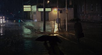 Movie still from “Stranger Than Fiction” (2006), directed by Marc Forster – A person walking down a street at night with an umbrella; Extreme Wide shot, High angle