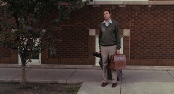 Movie still from “Stranger Than Fiction” (2006), directed by Marc Forster – A man standing on a sidewalk holding a camera and a briefcase; Wide shot, Low angle