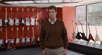Movie still from “Stranger Than Fiction” (2006), directed by Marc Forster – A man standing in front of a row of guitars; Medium shot, Over the shoulder angle