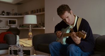 Movie still from “Stranger Than Fiction” (2006), directed by Marc Forster – A man sitting on a couch playing a guitar; Medium shot, High angle