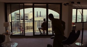 Movie still from “Stranger Than Fiction” (2006), directed by Marc Forster – A man standing in front of an open balcony door; Wide shot, Over the shoulder angle