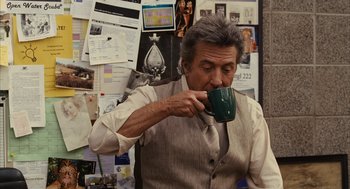 Movie still from “Stranger Than Fiction” (2006), directed by Marc Forster – An older man drinking a cup of coffee in front of a bulletin board; Medium shot, Over the shoulder angle